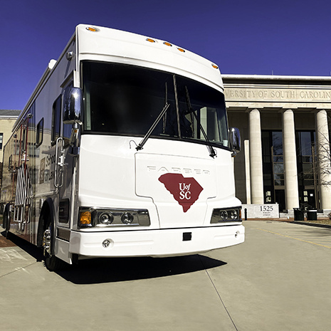 Close up of the front of the Palmetto Leader bus with the School of Law in the background.