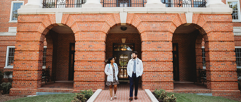 Pair of students in white coats leaving building three.