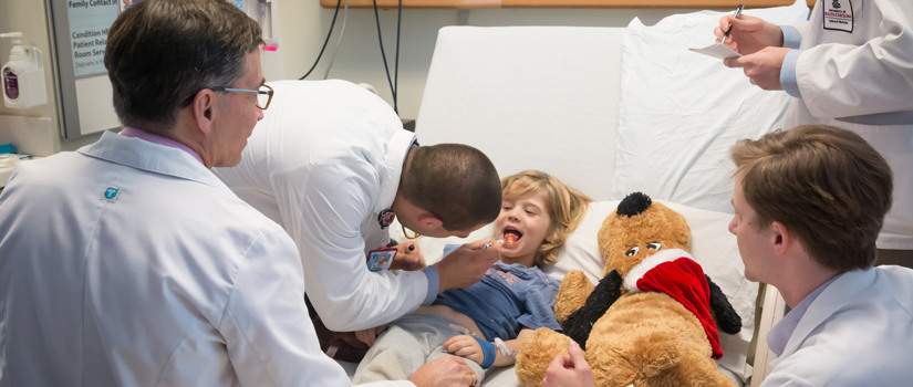 Doctors using a light to examine a young child's throat.