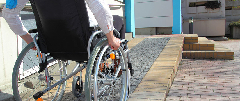 A man in a wheelchair maneuvers up a wheelchair ramp outside a home