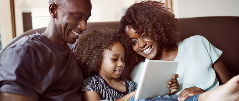 A child looks at her tablet with her father and mother.