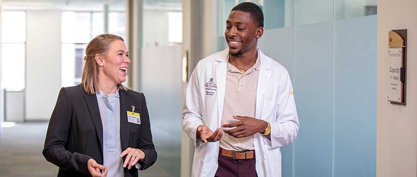 A black male med student walks and laughs with a staff member