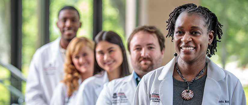 Black female doctor smiles at the front of a line of med students in white coats