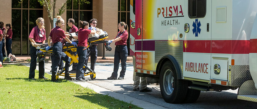 Student EMTs load a patient on a stretcher into an ambulance.