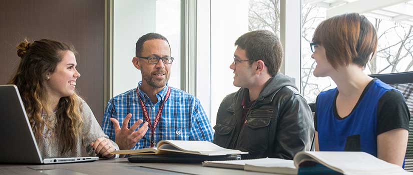 Professor talks with three pre-med students in light-filled conference room.