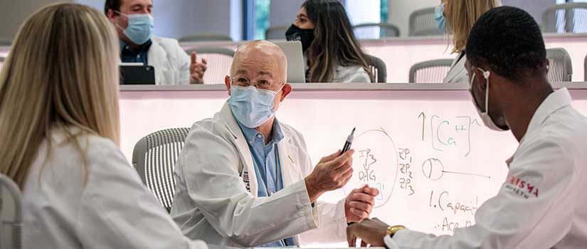 A doctor explains to students a problem written on an illuminated whiteboard.
