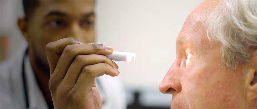 Medical student examines a patient's eye for pupil dilation.