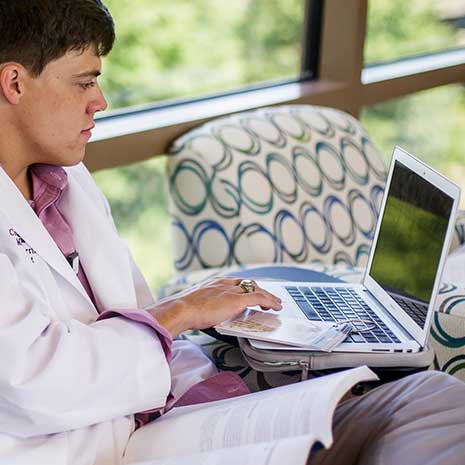 Med student in white coat works on a laptop. 