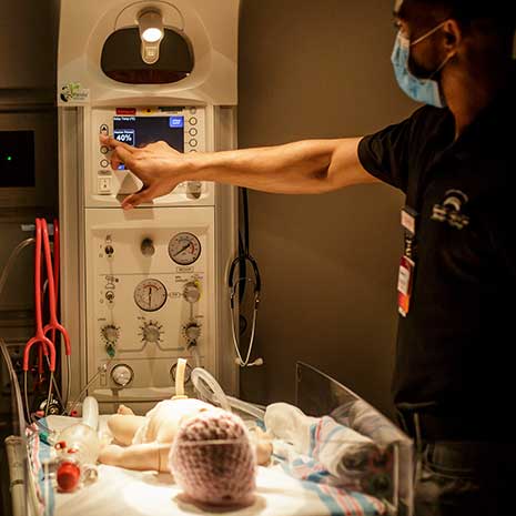 Med student adjusts infant warming unit in simulation lab.