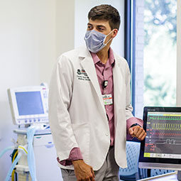 A male med student in a white coat checks patient monitors in a sim lab..