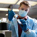 Student in labcoat fills a pipette.