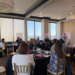 A group of people gathered around a table listening to a presentation.