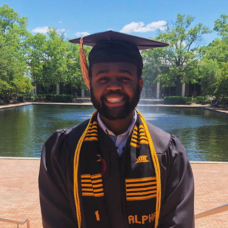 Image of Kendall Little in his cap and gown in front of the Thomas Cooper Library fountain