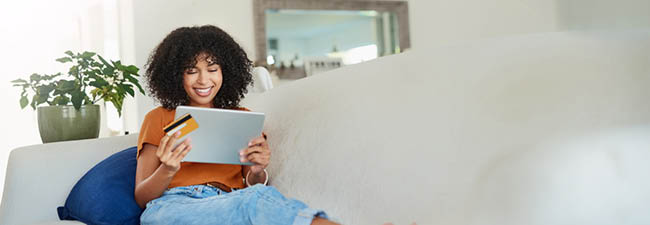 Image of a woman sitting on a couch with a tablet and a credit card