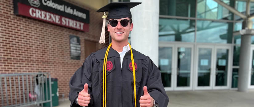 Image of Connor Larson in cap and gown with two thumbs up
