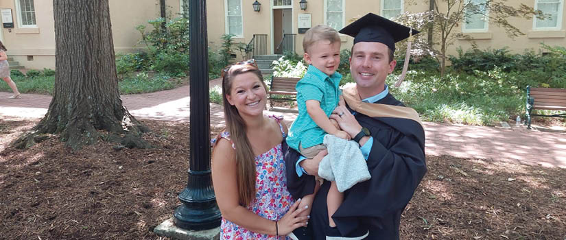 Image of Sterling Davidson in his graduation cap and gown with his wife and son