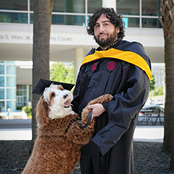 Image of Jordan Montiel in his graduation gown with his dog in his graduation cap