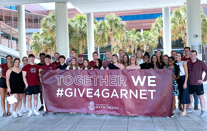 group of students standing in Moore School courtyard, holding a banner that reads: Together We #GIVE4GARNET