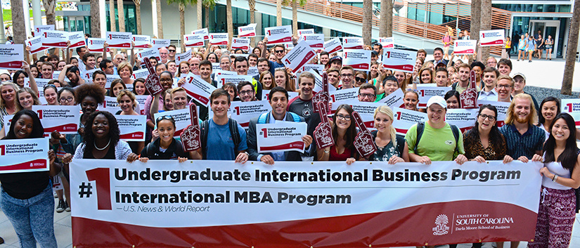 Undergrad IB students holding No. 1 IB program signs in the Palmetto Courtyard