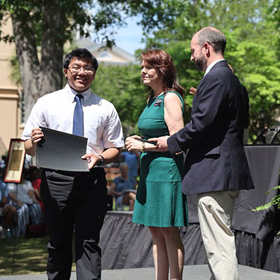AllanDave walking across the stage holding his award for Outstanding Undergraduate Leadership
