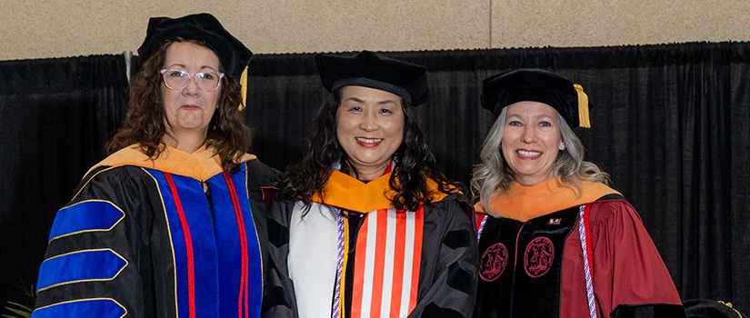 Ann Cook posing on graduation stage with two professors
