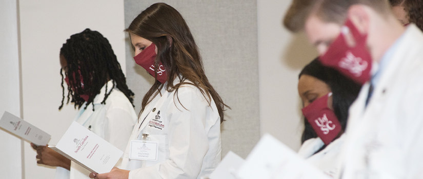 Students in white coats reading from program
