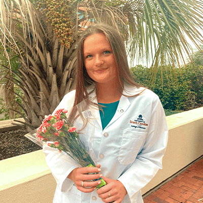 Student in white coat holding bouquet of flowers