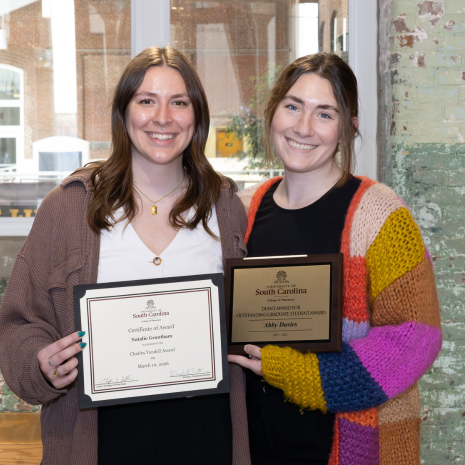 Two graduate students holding award plaques