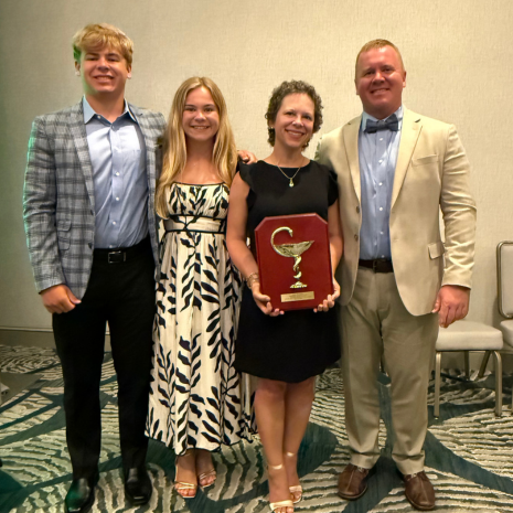 Family of four with adult female holding award plaque