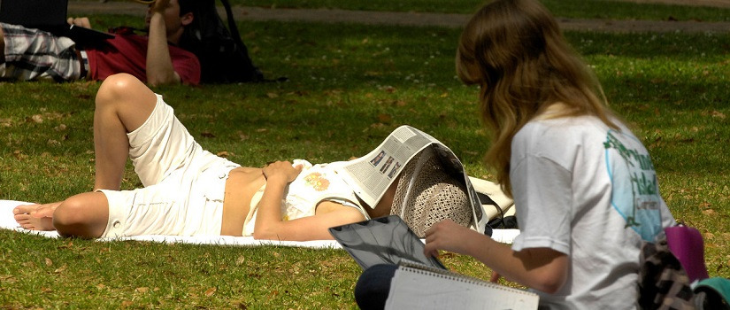 Students in the park. One is napping with a newspaper over his head.