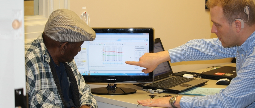 Communications Sciences and Disorders faculty member pointing out graphical data on a computer screen to an older gentleman