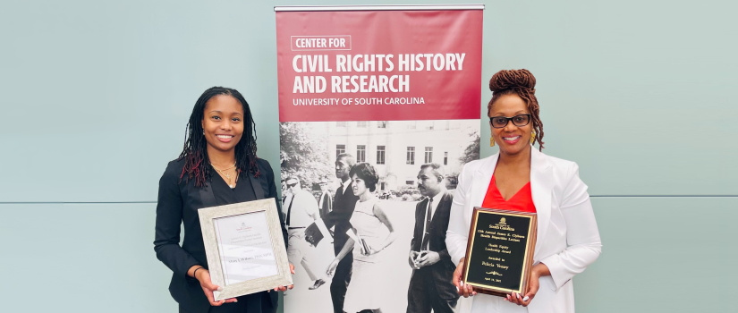 Two women standing with awards in front of a banner commemorating civil rights history