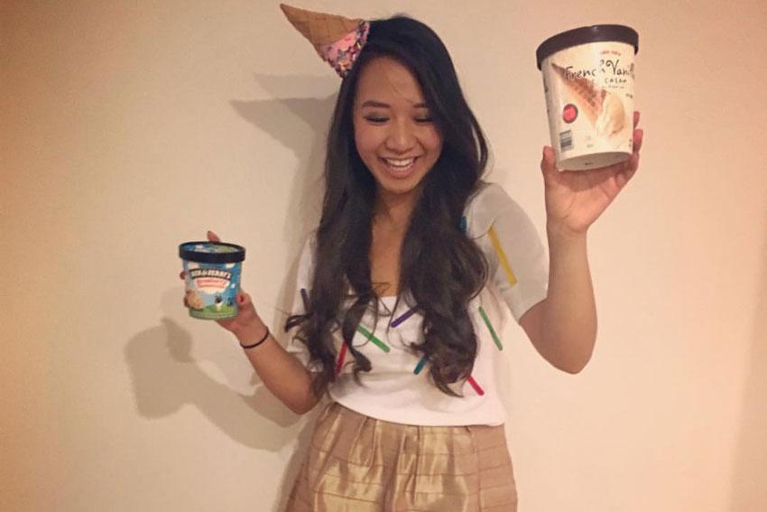 A girl dressed as an ice cream cone holding a contain of ice cream.