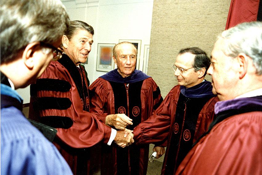 Ronald Reagan, Richard Riley and Strom Thurmond in commencement attire, shaking hands.