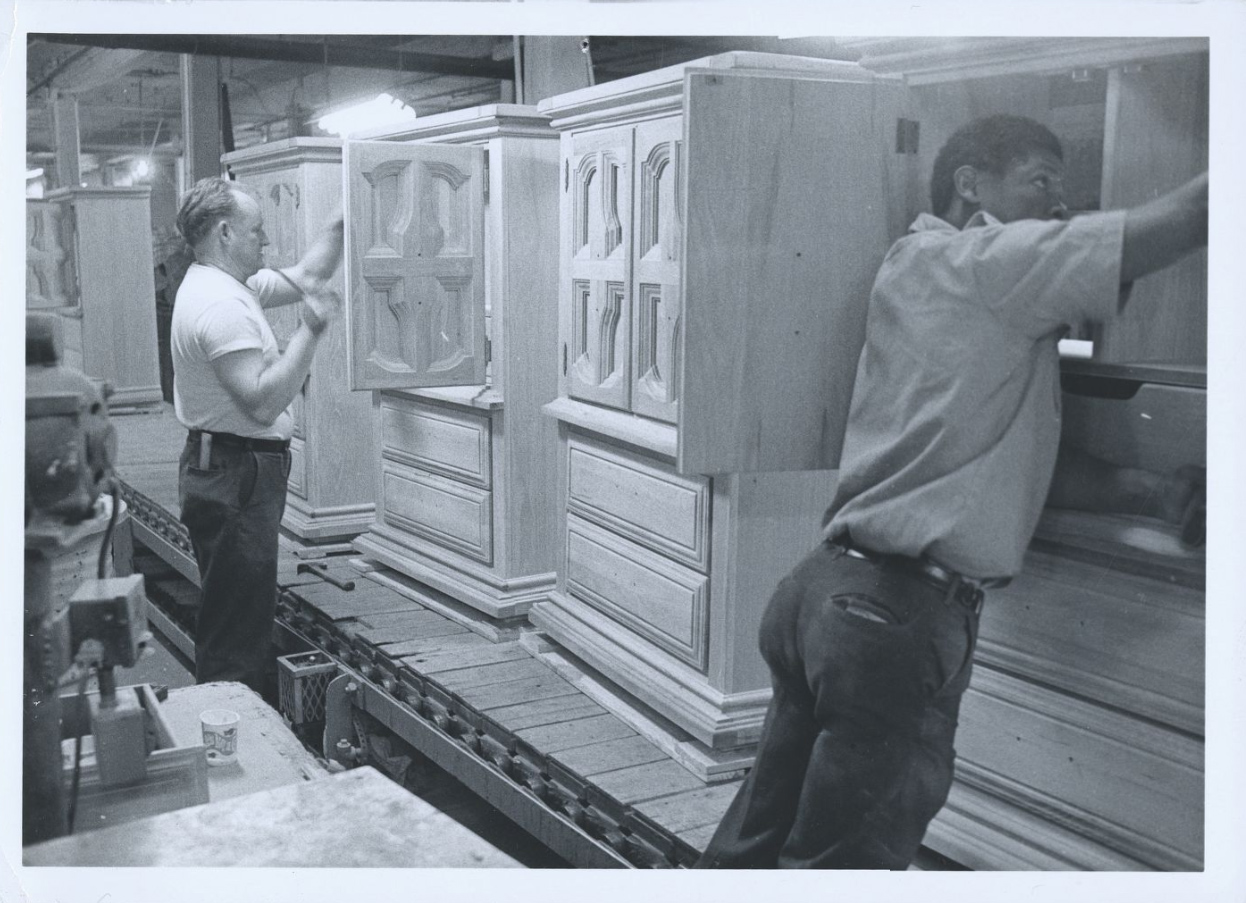 Employees build solid wood armoires on the factory’s conveyer belt.