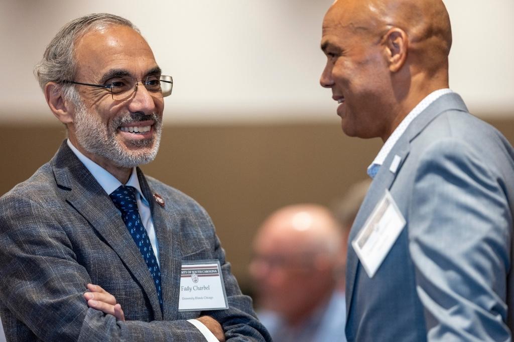 Two men in suits smile and speak with one another. 