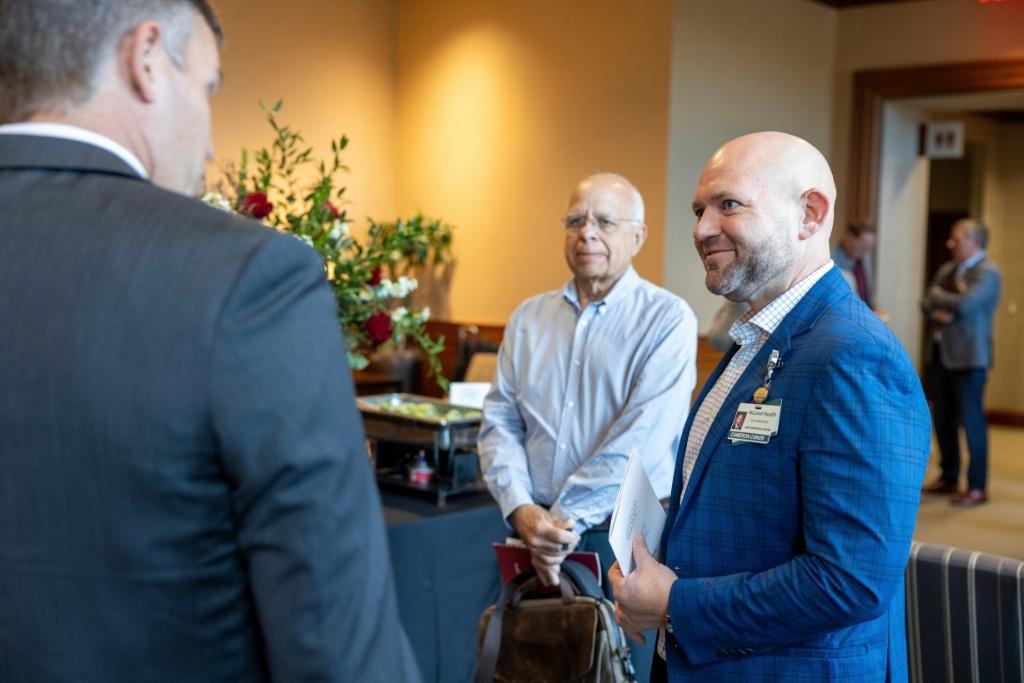 Three men in suits speak together in a conference hall. 