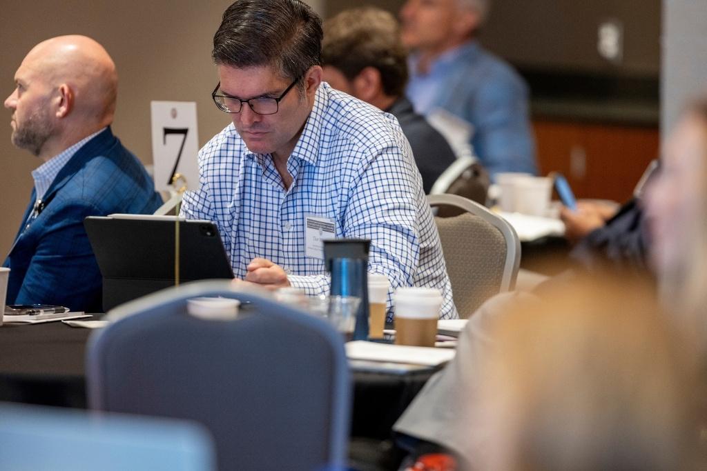 A man in glasses sits at a table and works on a laptop.