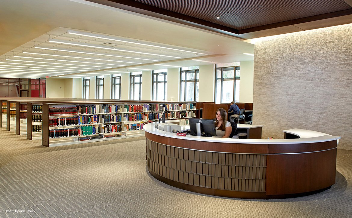 Woman at the front desk of the Law Library with shelves of books in the background.