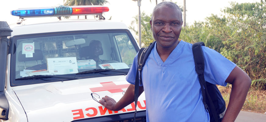 Nursing professor in blue scrubs stands in front of an ambulance