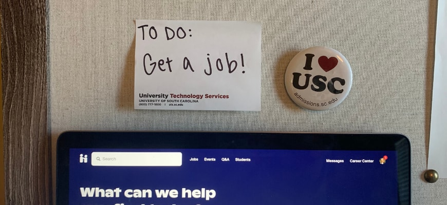 The top of a laptop with the Handshake website homepage open. Above is a post it not that says "to do: get a job!" and a button that says I *heart* USC