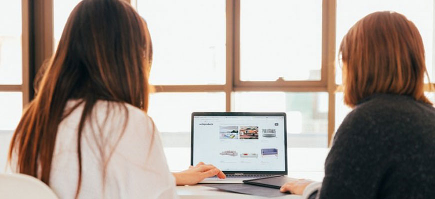 two women sit in front of a computer screen