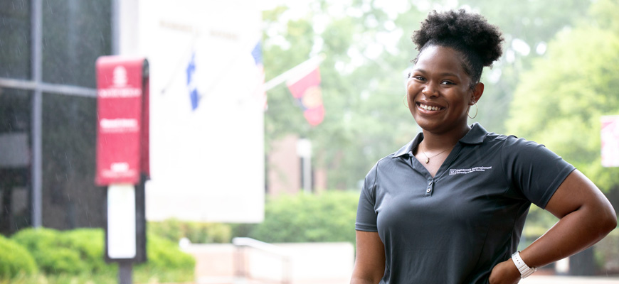 Shawnese Cleveland stands smiling outside in front of the university's Russell House.