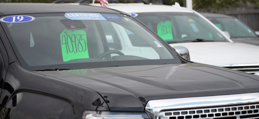 A car on a sales lot with a green price sticker on the windshield with other cars in the background.