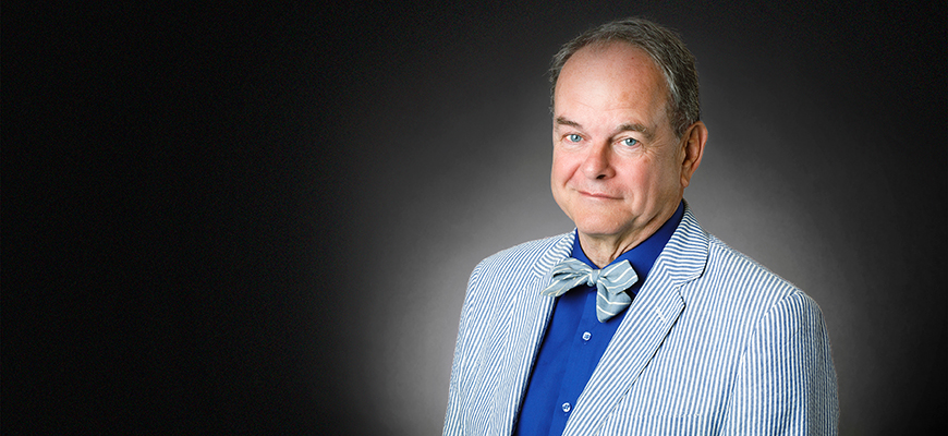 David Shields stands smiling against a dark gray studio background. 