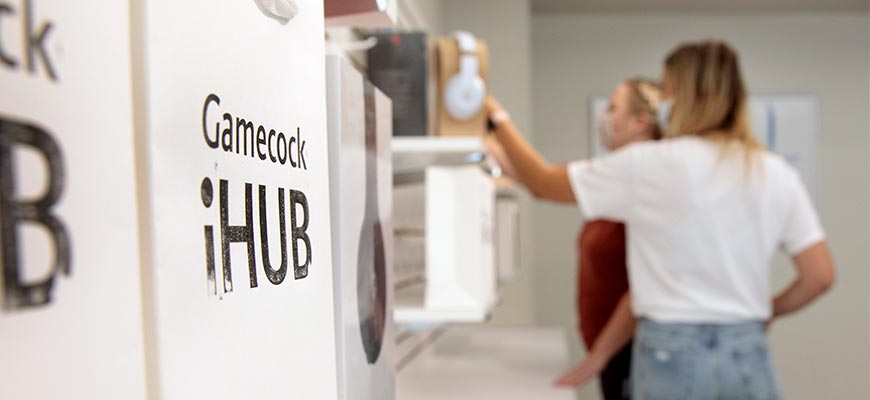 A shopping bag sits on a counter with the Gamecock iHub logo while two people browse the store in the background. 