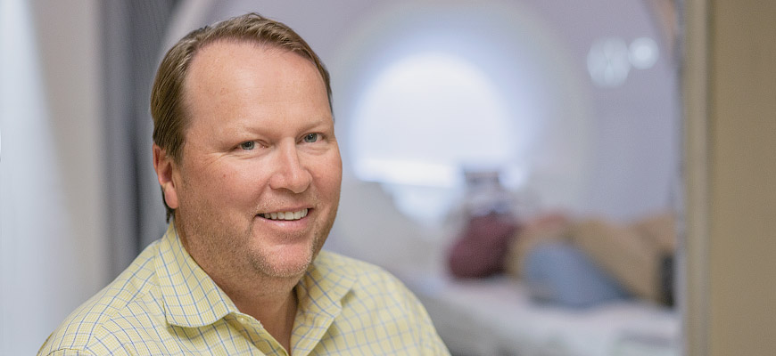 Julius Fridriksson smiles into the camera, while behind him is body scanning machinery