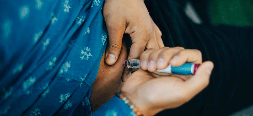 Photo of a person't midsection as they inject insulin with a syringe.