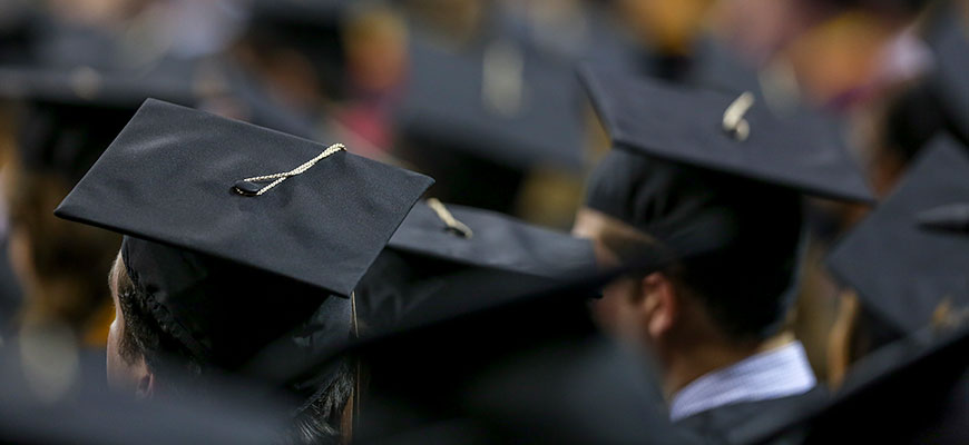Students in mortarboard caps sit in the Colonial Life Arena