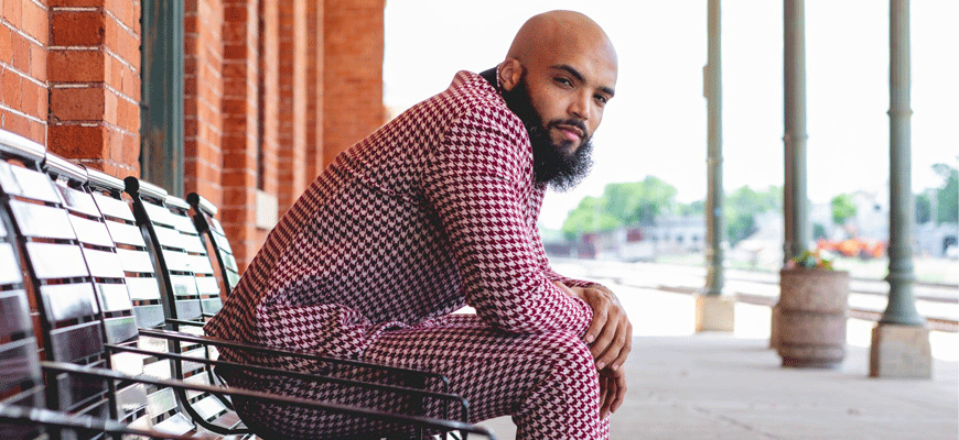 Composer Marcus Norris with shaved head and beard in a maroon houndstooth suit.